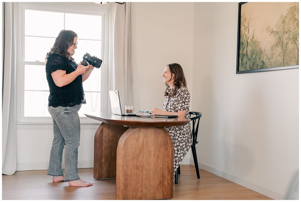 Behind-the-scenes photo of a brand photographer capturing a client at a desk during a creative branding session in a well-lit room.