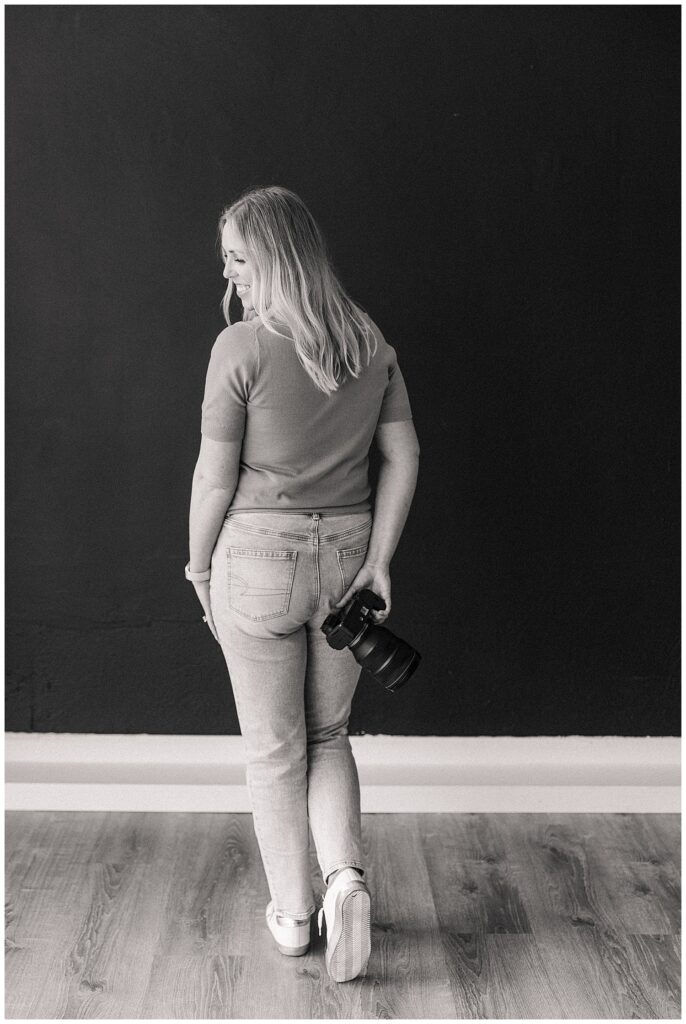 Black and white photo of a female photographer holding her camera confidently, highlighting a timeless brand identity.