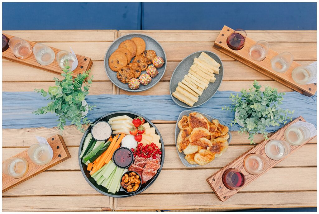 Top-down view of a luxury picnic setup with charcuterie boards, fruit, and wine on a wooden table—ideal for food, travel, or event planning brands.