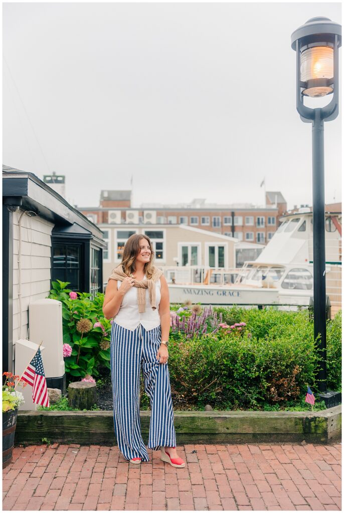 Travel brand photo of a woman in striped pants and sunglasses enjoying an iced coffee outside a charming coastal café.