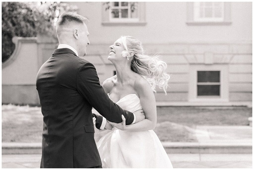 Joyful black-and-white photo of bride and groom dancing outside Great Marsh Estate.
