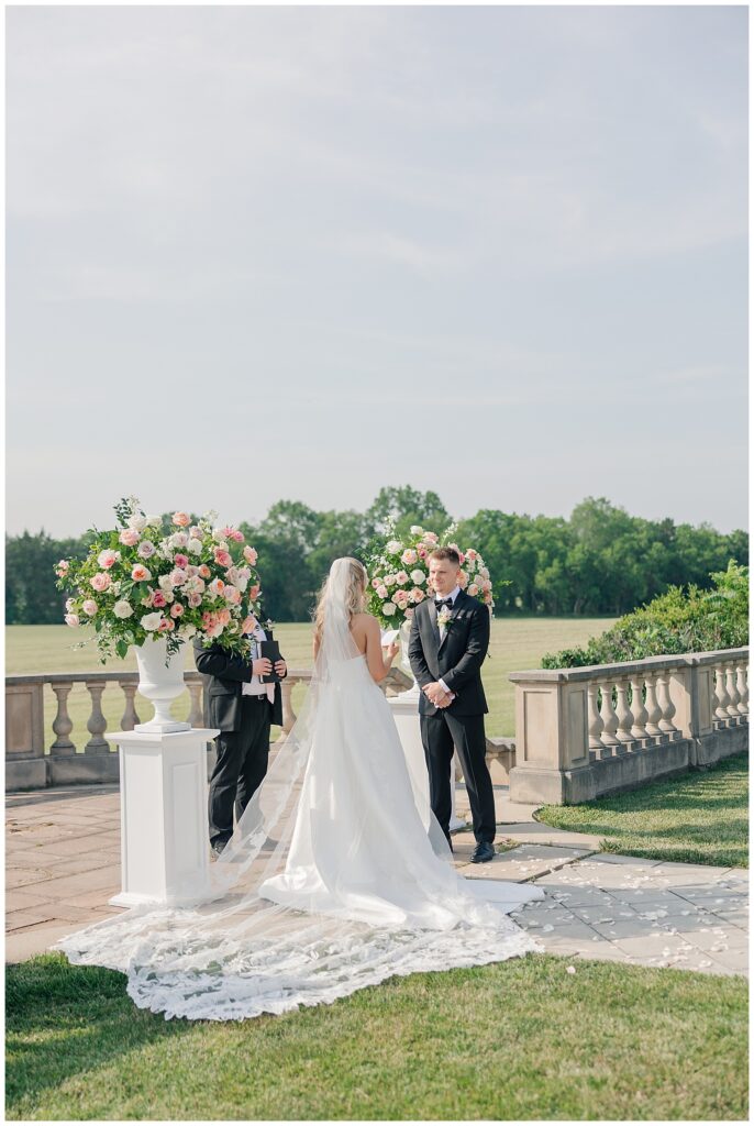 Bride and groom standing with their officiant during a romantic outdoor ceremony on a stone terrace overlooking the countryside.