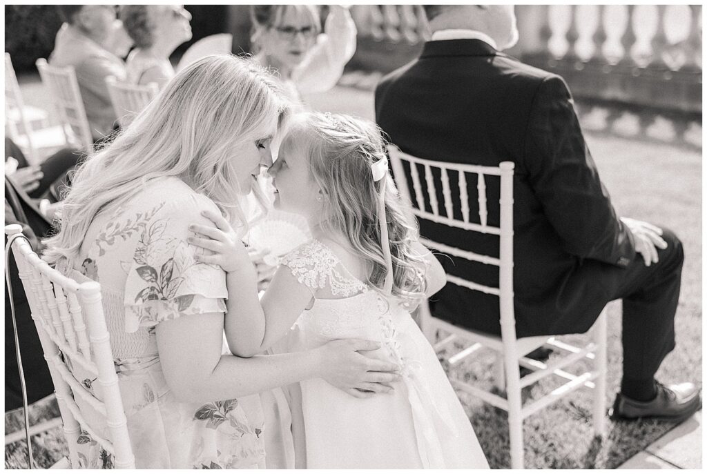 Candid moment of a young flower girl being hugged by a guest during the wedding ceremony.