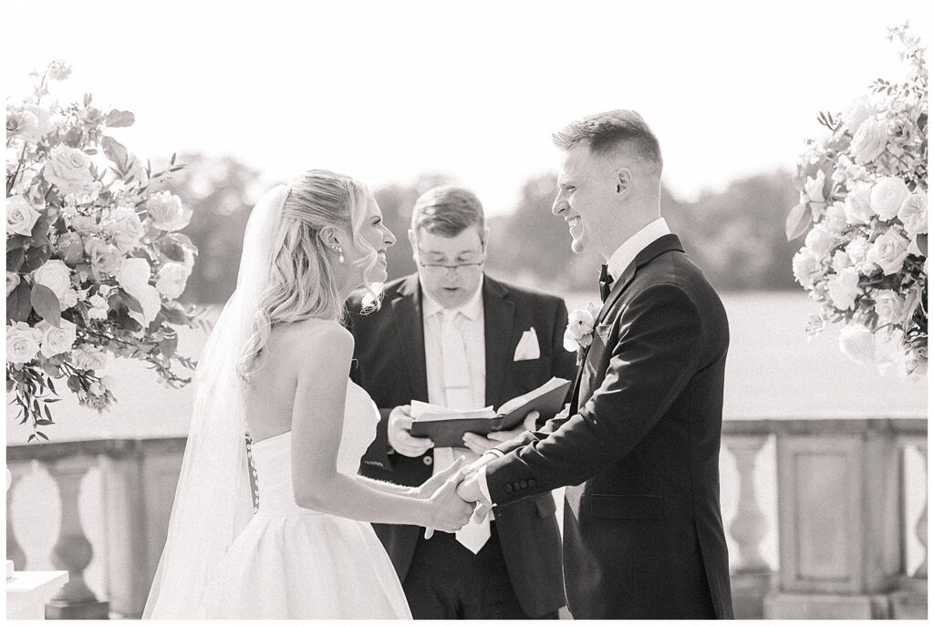 Bride and groom exchanging rings during an emotional outdoor ceremony, with the officiant smiling behind them.