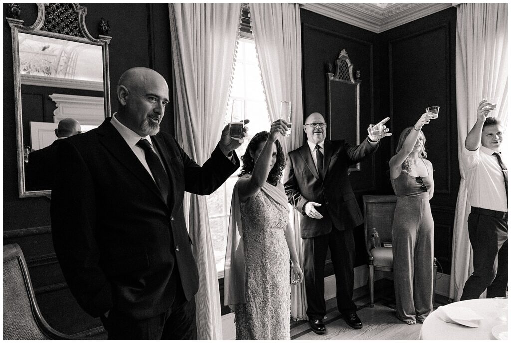 Candid black and white photo of guests raising glasses in a celebratory toast indoors.