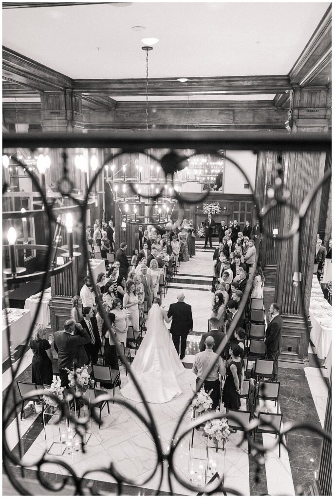 Bride walking down the aisle during wedding ceremony at Hotel Morgan, viewed from above the grand staircase.