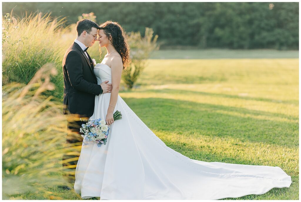 Romantic wedding portrait of couple standing close together in an open field, bride holding pastel bouquet