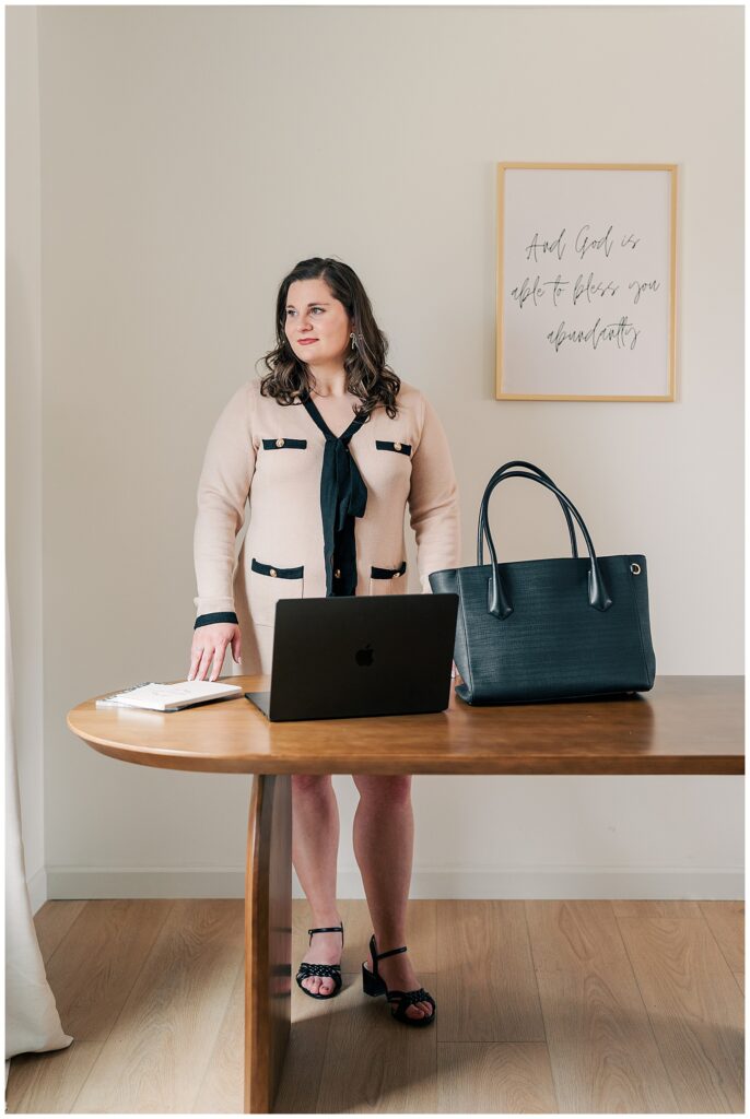 Female business owner standing at a table with a laptop and handbag during a professional brand photoshoot.