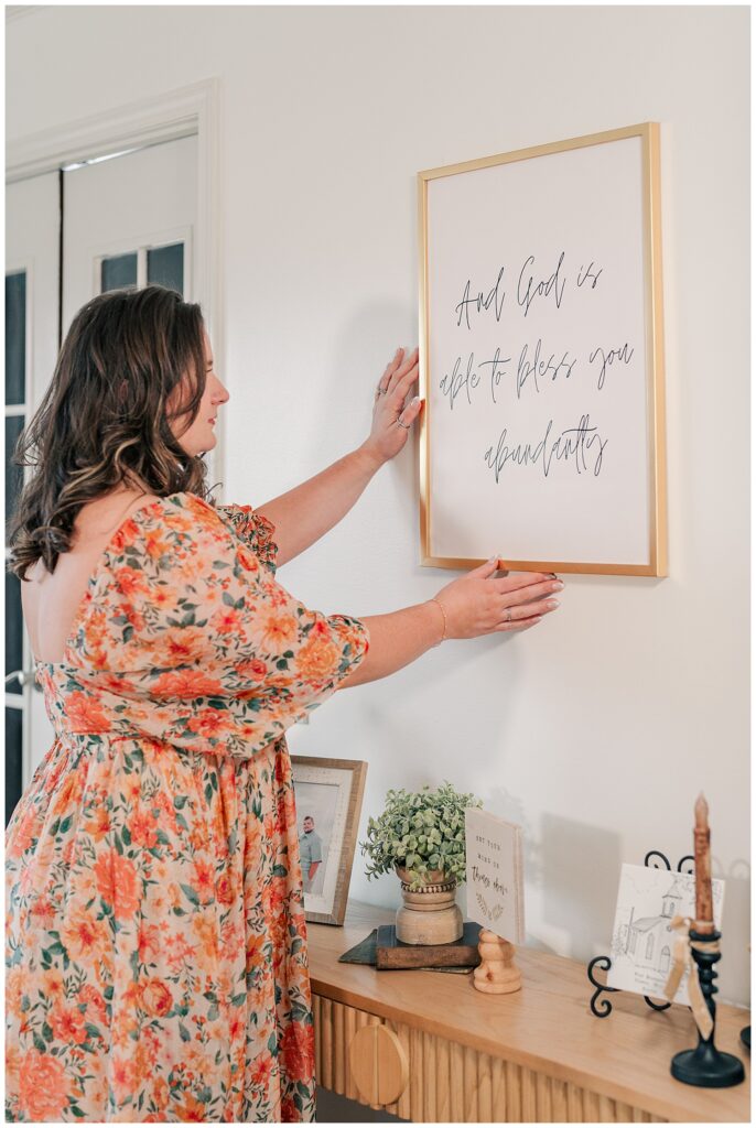 Woman adjusting framed wall art during a styled brand photoshoot in a bright home studio. Zoe Evans Photography