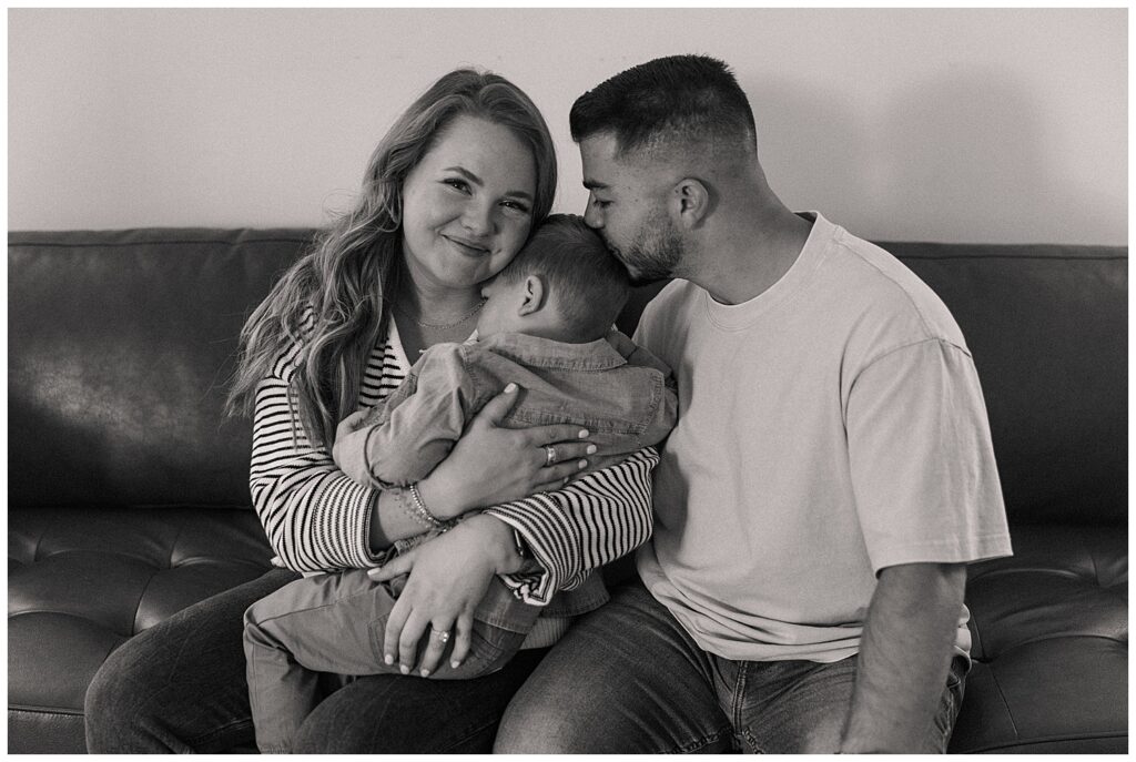 Black and white photo of Liz cuddling her son as her husband kisses her on the forehead—showcasing love, legacy, and family as the foundation of her brand