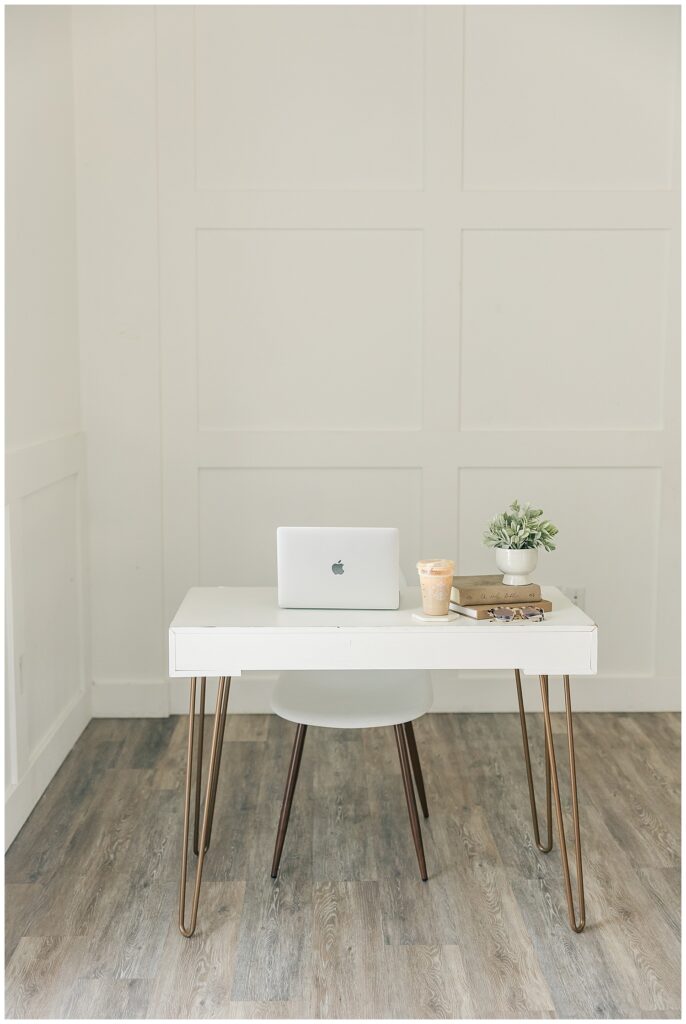 Clean flat lay of a laptop, coffee, and notebooks on a white desk, styled for a modern and minimal VA brand aesthetic.