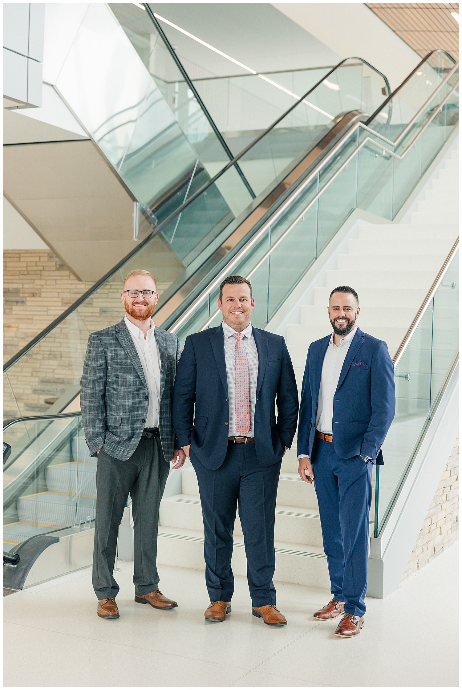 Corporate brand photo of three male professionals in business attire posed confidently in front of a modern glass staircase during a team branding session with Zoe Evans Photography.